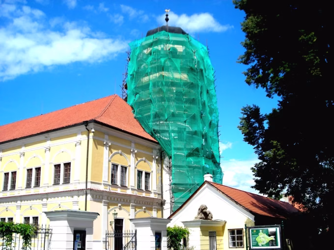 Věž zahalená lešením se sítí za historickou budovou